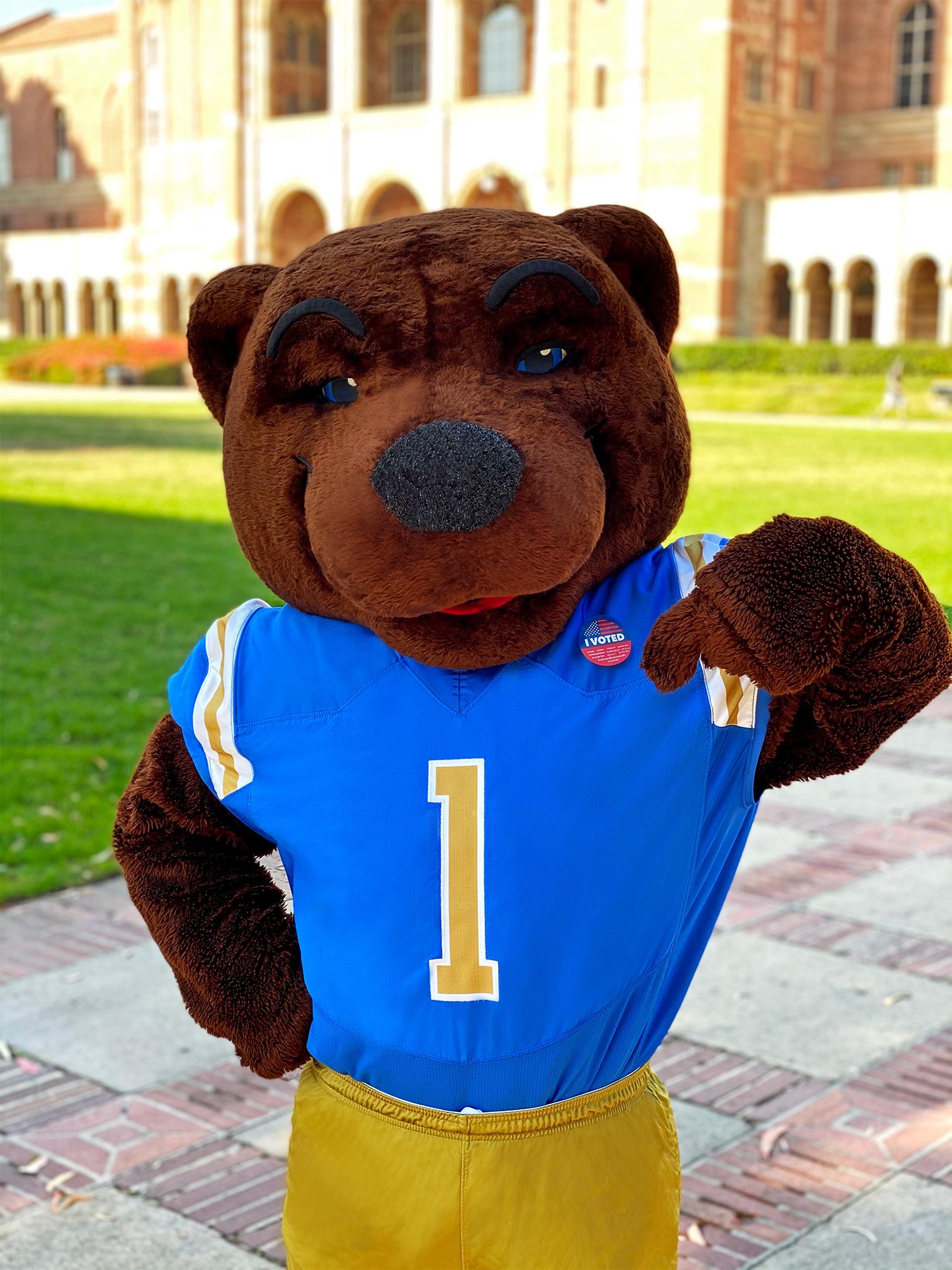 Picture of Joe Bruin in front of Royce Hall pointing to an "I voted" sticker on his UCLA jersey. 